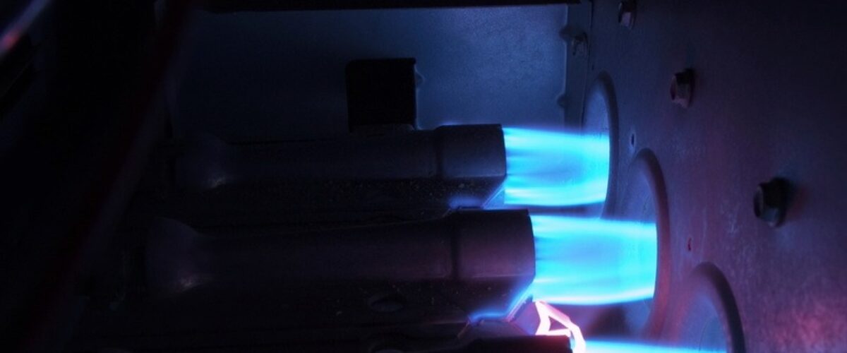 Three natural gas burners with bright blue flames inside an operating gas furnace.